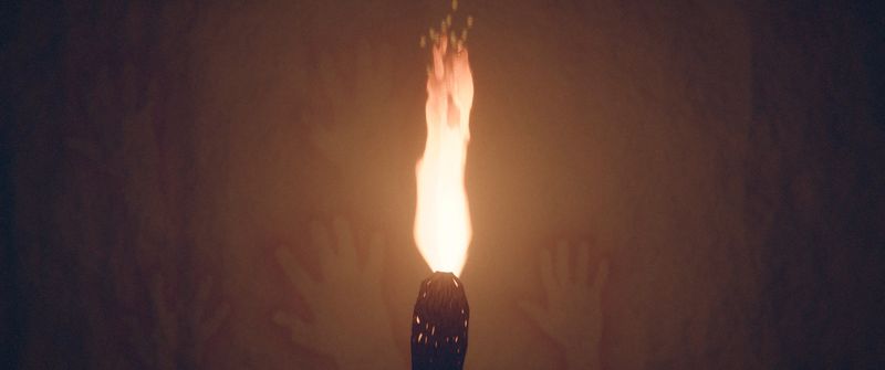 A torch flame in front of a cave wall with hand stencils.