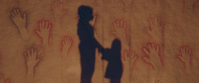 The shadow of a mother holding her small daughter's hands; the girl looks up at her.
