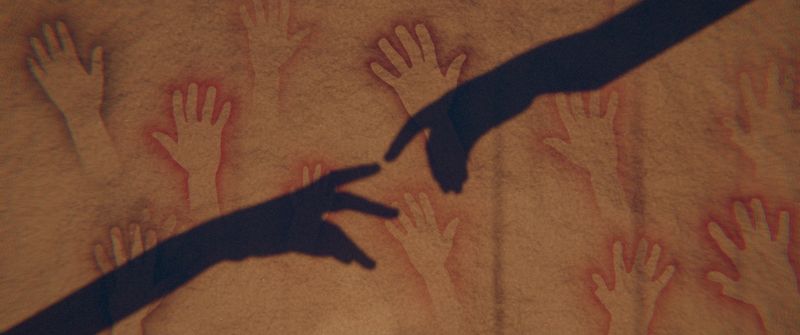 The shadows of two hands reaching toward each other across the wall.