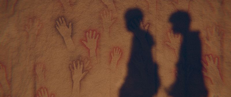 Shadows of two people walking past the hand stencils.